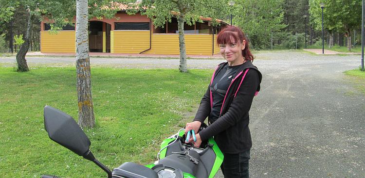 Sharon smiles at the camera standing next to he bike on a campsite in Spain