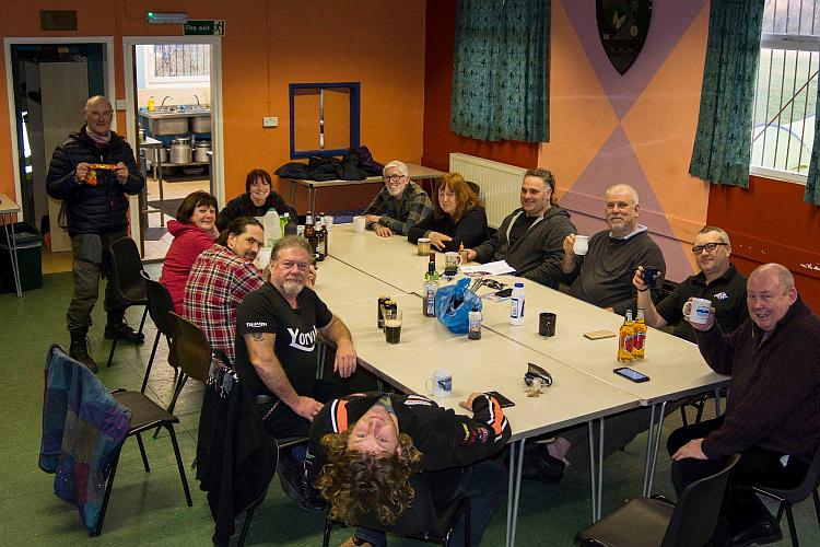 A group of motorcyclists around a table laughing and smiling at the camera