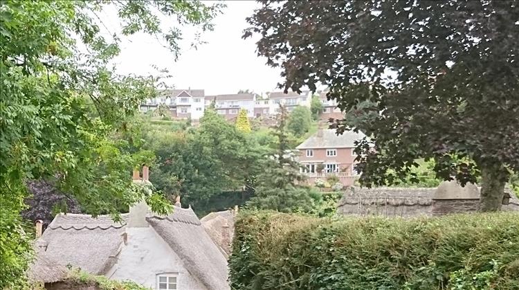 Behind the thatches and trees up the hill are modern houses spoiling the illusion