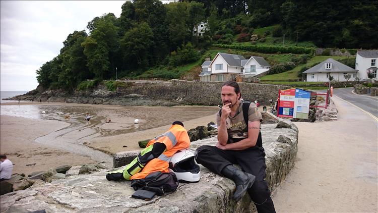 Ren sits on the sea wall with a thinking expression and stroking his chin at Salcombe beach