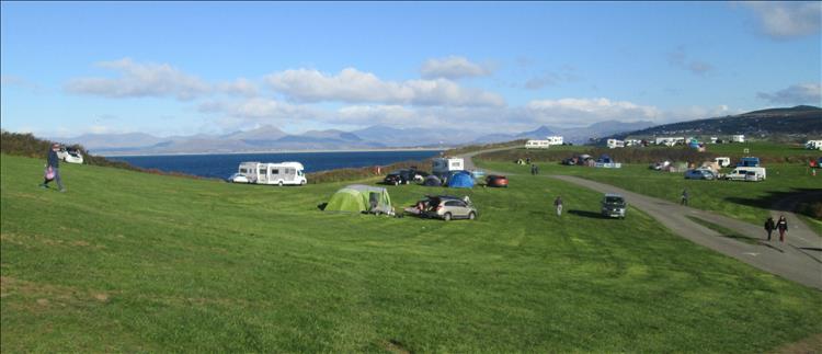 Tents and caravans on a site with the sea and mountains in the background