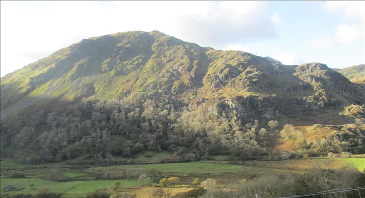 A steep green hill rises from a flat valley floor with low sunlight enhancing the grandeur