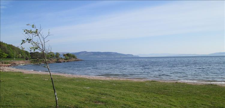 grass runs to a shallow beach with mountains in the misty distance across the waters