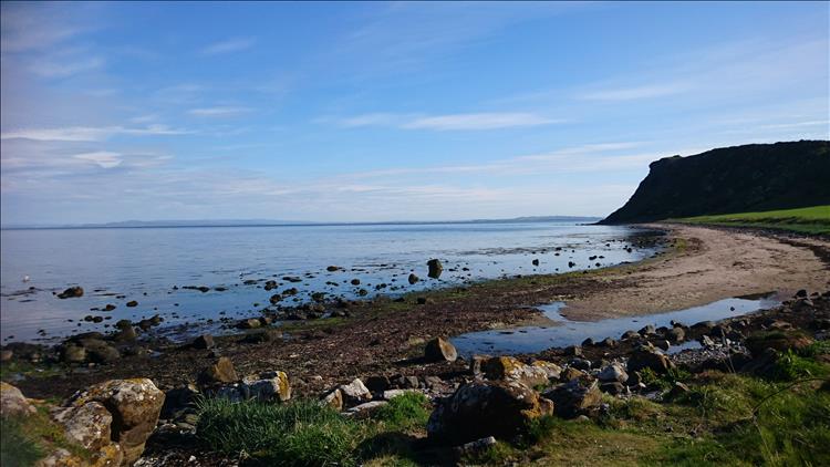 A curved beach, steep hills forming a bay, rocks and totally calm waters at Bracken Bay