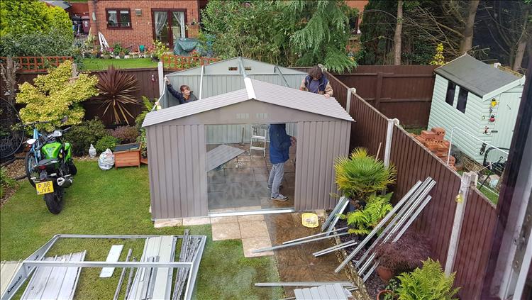 Looking down from a window we see several people holding on to the shed as it's being put up