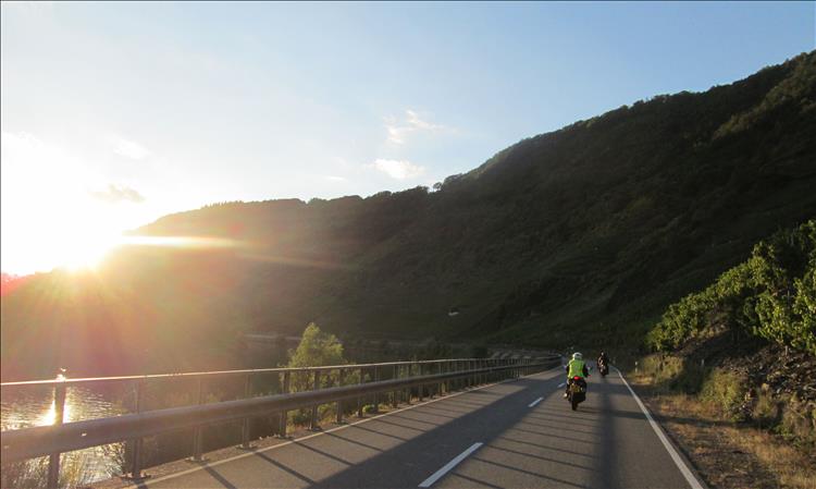 Motorcycles, clear skies, sun and steep valley sides as 3 motorcycles ride along side the river Mosel