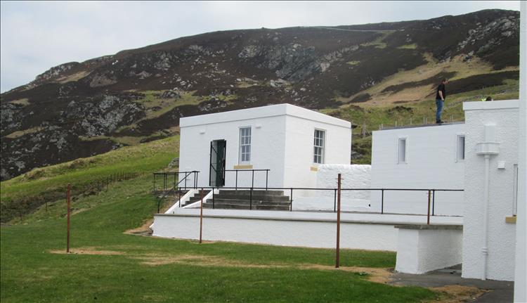 A worker on the roof of the crisp white buildings at the lighthouse, steep hillside behind