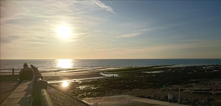 The sun low in a hazy sky over the sea and the beach at Ambleteuse