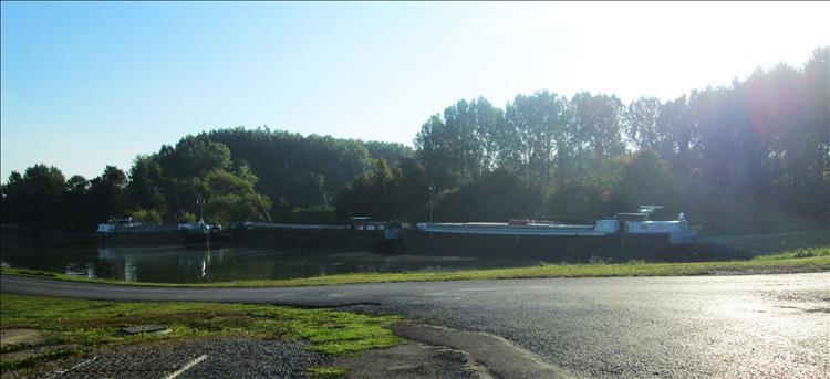 Large broad canal boats on a calm stretch of water in Arleux