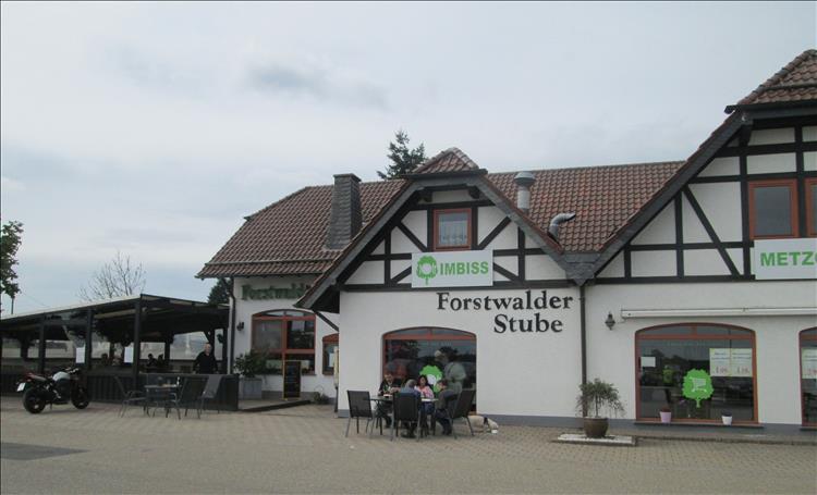 A white building with steep roof, tables and chairs outside and even a motorcycle