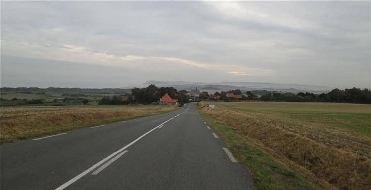 Although the skies are grey we look down a road to fields, distant hills and clumps of trees in Kent
