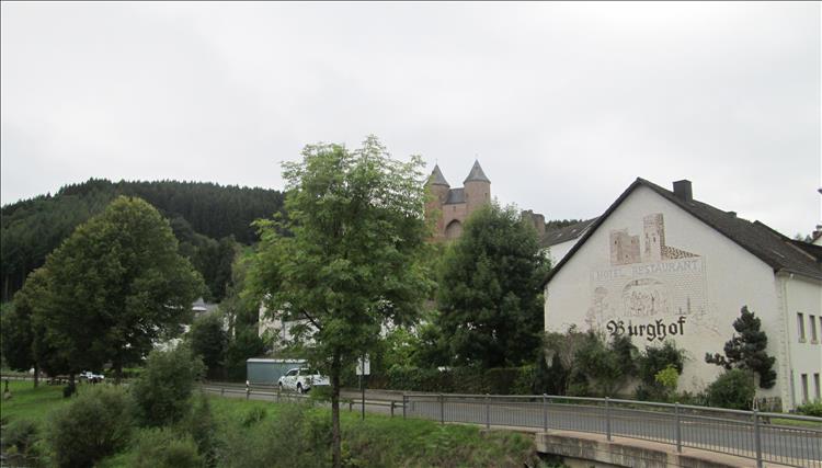 A Germanic spired castle behind trees and building in Murlenbach