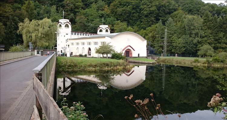 A large white building set among trees and a calm small reservoir. The building is stylish and quite old