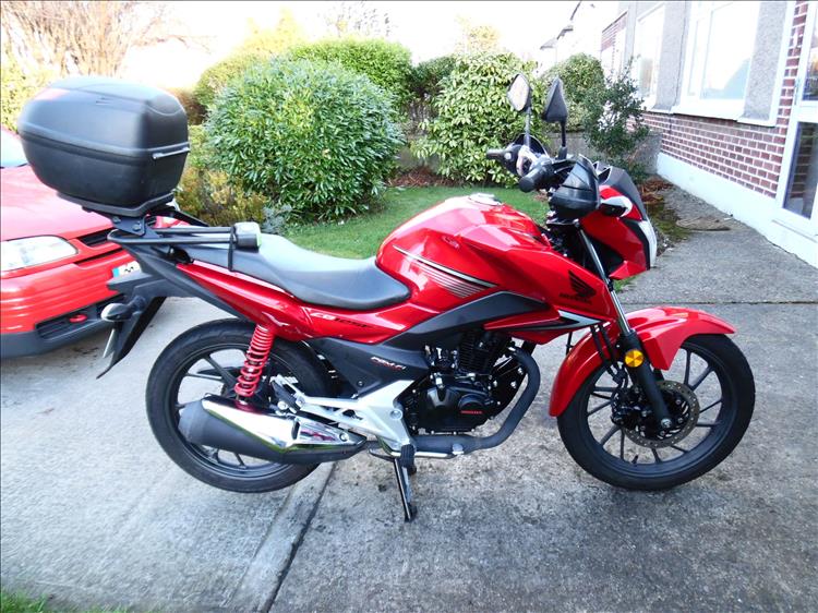 A bright red Honda CB125F with top box and handguards