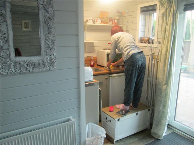 Sharon stand on a box to reach the top of the oven while making tea