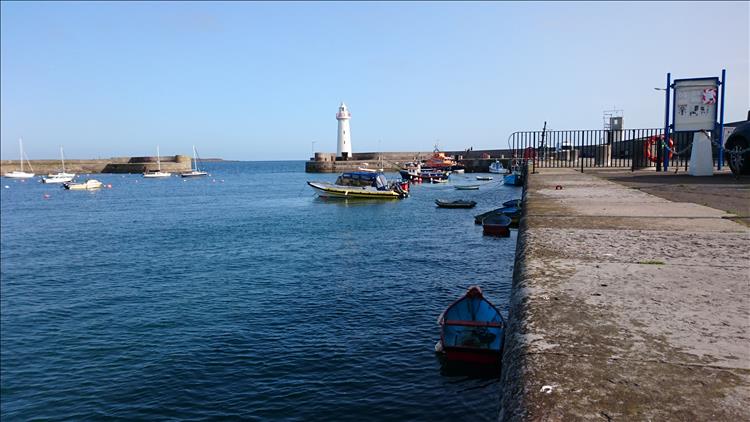 The stout bright white lighthouse on the entrance to the large sturdy harbour wall