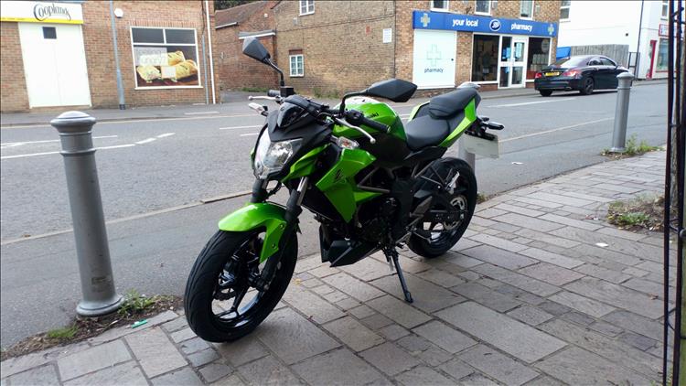 A kawasaki Z250SL in green outside some shops