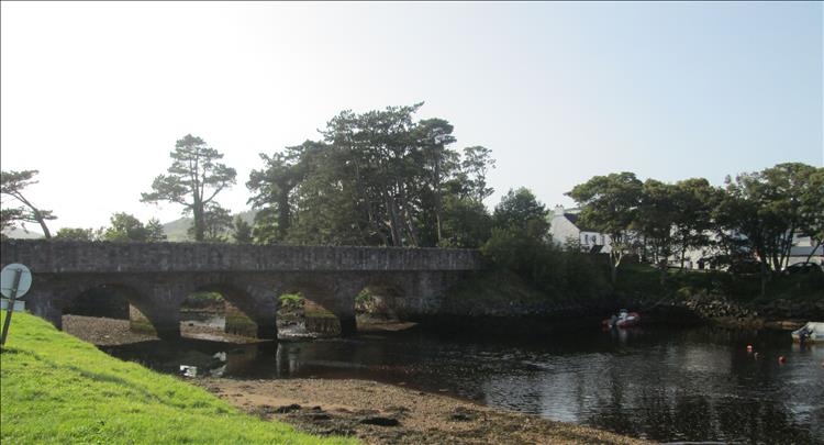 An old stone bridge with several arched spans crosses the gentle river at Cushenden