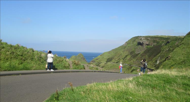 A tarmac lane leads down through green hillsides with the sea in the distance