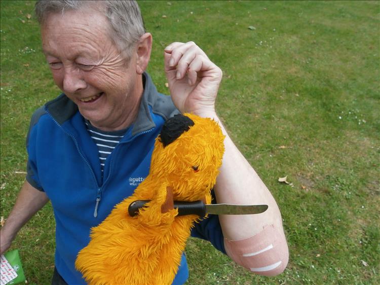 The hand puppet sooty has a knife and is pretending to do surgery on Ironsides Elbow