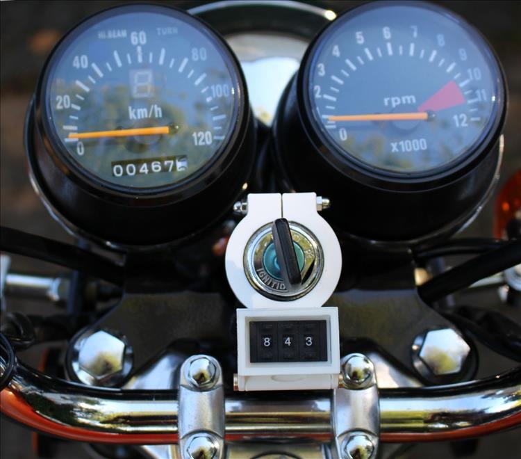 The meter in a 3D printed plastic housing, attached to the key barrel of the motorcycle
