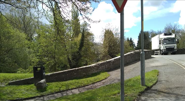A small bridge over a little river, trees starting to grow leaves and lush deep grasses