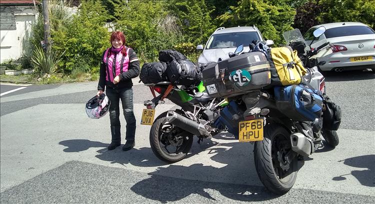 Sharon smiles in the sun next to the heavily laden motorcycles while on the road