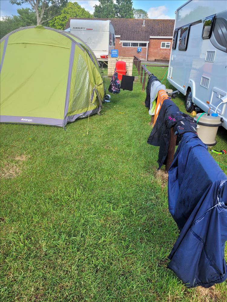 By the tent is a low wooden fence covered in clothes and motorcycle kit drying out