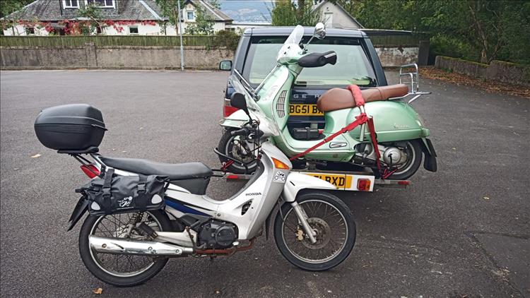 The lime green Vespa is mounted on a rack behind he Land Rover, the Innova is in front