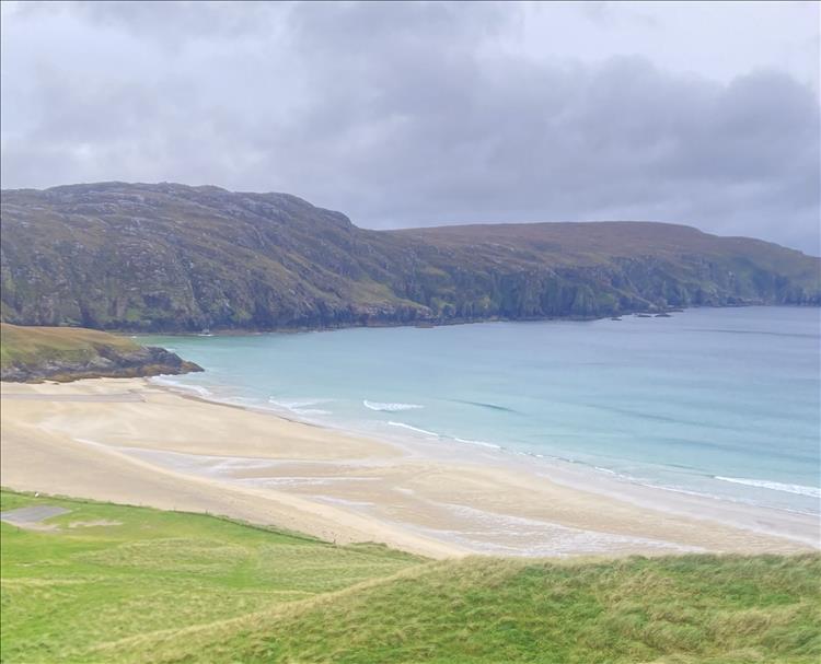 Looking down across fields and hardy grasses we see a huge sandy beach and towering bluffs