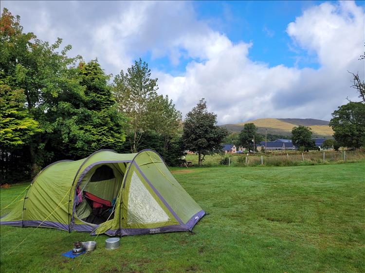 Above the tent and the trees we see blue skies as well as heavy clouds