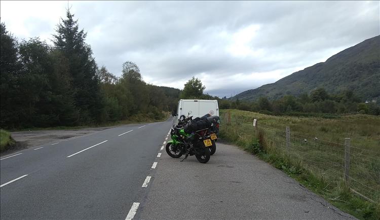 The road goes off into the trees and mountains of the Scottish Highlands