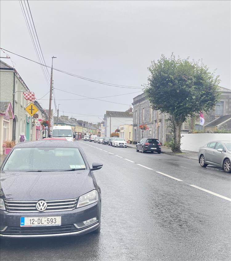 A car, a street, houses and shops, in the pouring rain