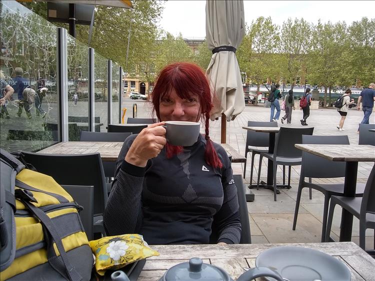 Sharon holds up her coffee cup in a cheers manner at the cafe on the market square