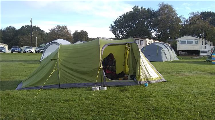 Sharon sits face down looking at her phone within the porch of the tent