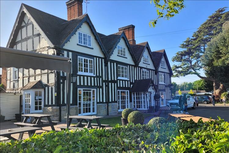 A large timber framed building set in a modern car park with gardens