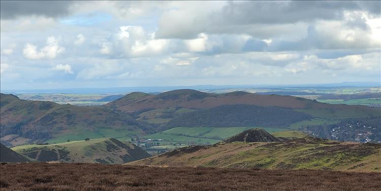 We look across angular hills and big skies to open countryside in the distance
