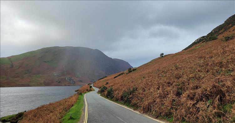 A bulbous towering rocky hill, steep sides leading to a lake, mist and a narrow road