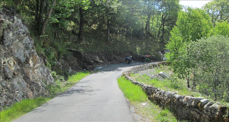 A narrow lane, steep rocks, dense trees and a stone wall in the Highlands of Scotland