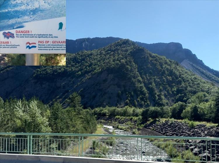 A pretty river under a bridge in the alps and a sign warning of hydroelectric damn upstream may cause floods
