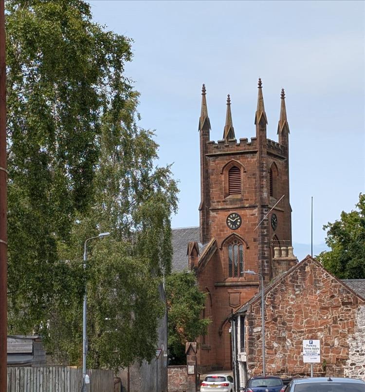 A dirty red sandstone church among houses, trees and cars at Mauchline