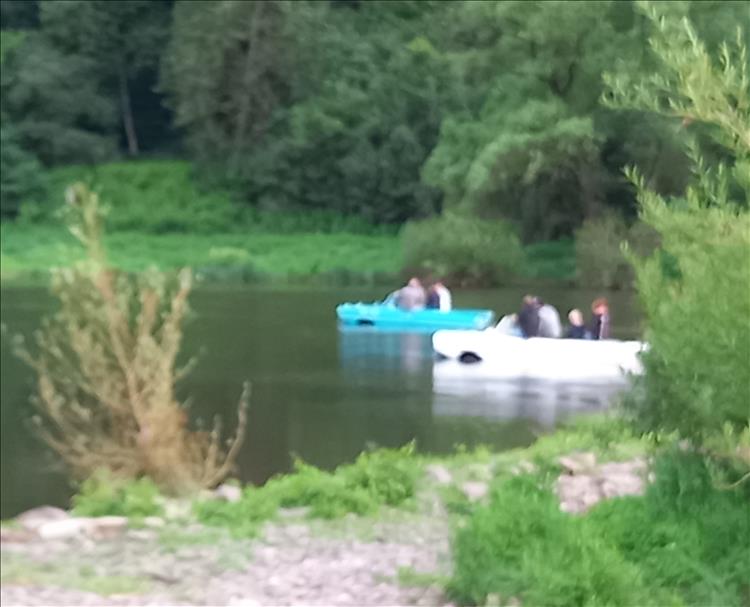A very blurred shot of a white and a blue amphicar coming through the river