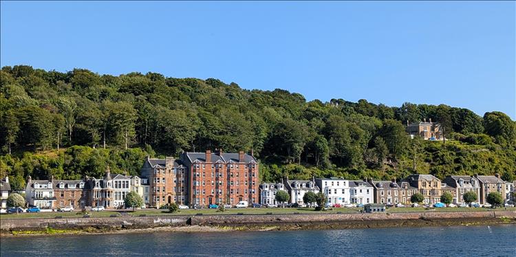 Houses nestled in trees and the shore of the Firth of Clyde seen from the Bute to Wemyss bay ferry