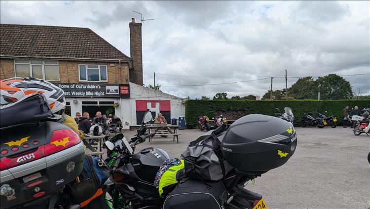 Cafe H, a cafe in a block of shops with a number of motorcycles, riders and benches outside