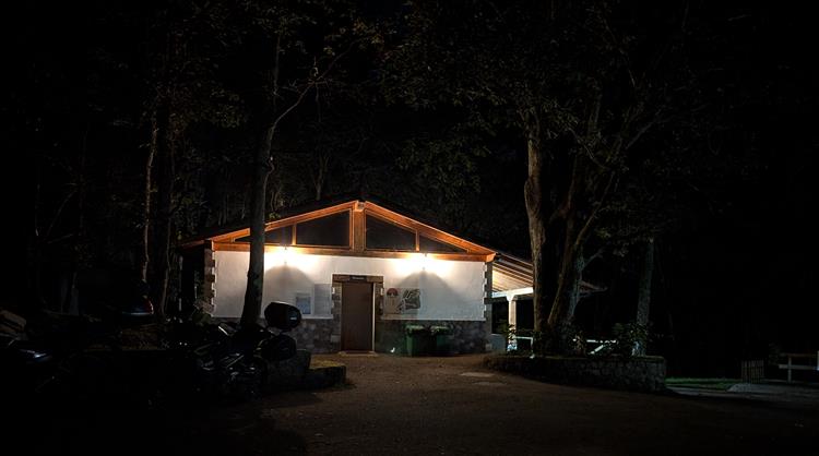 In the dark a low building is lit and we can make out a few trees and perhaps a motorcycle