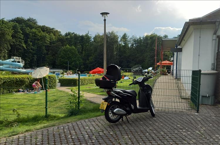 Trees, a pool with waterslide, grass, campers, toilet block and Bogger's scotter