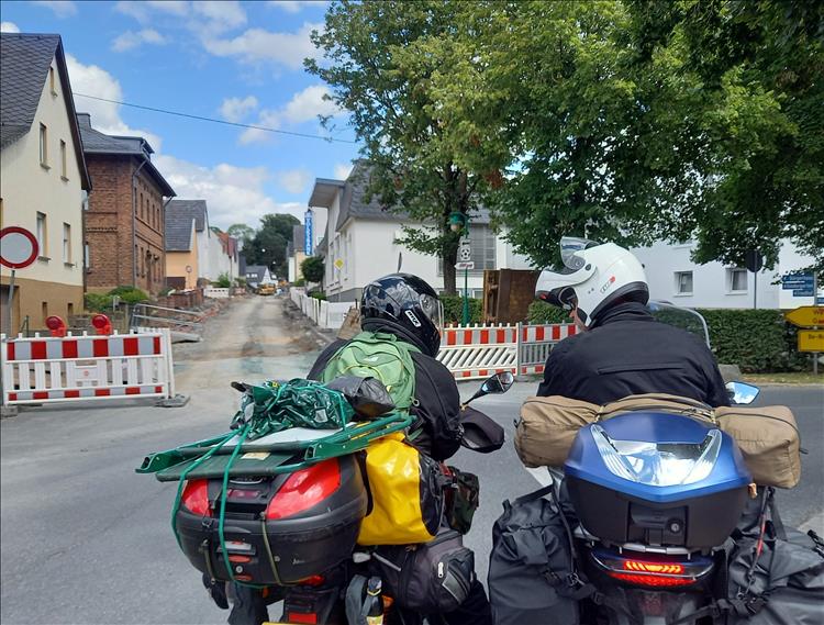 2 small bikes with luggage, a closed road and the riders discussing routes