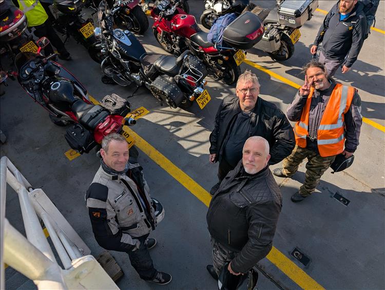 The lads, the riders looking up at the camera and stood beside the bikes on the deck of the ferry