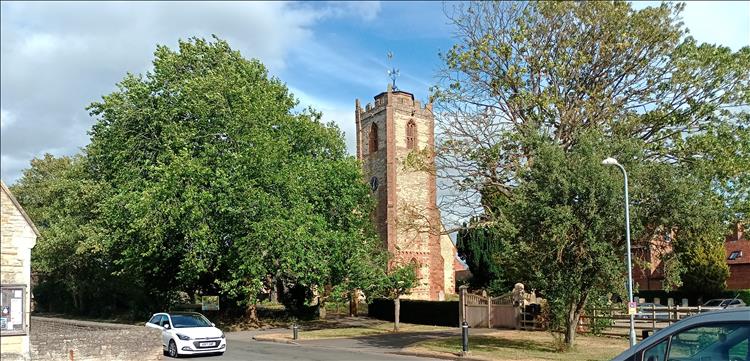 A church on a sleepy lane with trees, a couple of parked cars and all in the sun