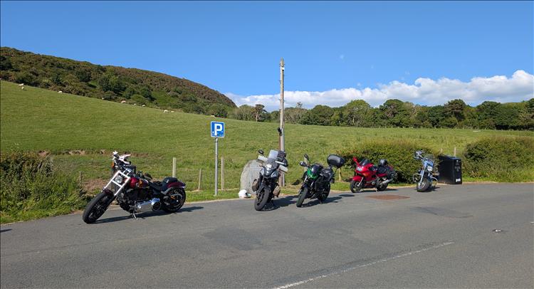 Bikes in a layby, green hills, sheep and the road. The road looks quite flat